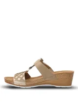 Sandalias de plataforma baja con diseño de tiras cruzadas en color beige y dorado. Presentan una tira superior con cierre de velcro y una tira frontal con detalle de calados geométricos y pequeñas tachas metálicas. La plantilla es acolchada y la suela tiene textura tipo yute.