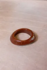 Pulsera rígida de resina con diseño orgánico y acabado brillante, disponible en colores marrón, gris y naranja.