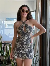 Vestido corto negro con estampado de plumas doradas, escote en V, breteles finos cruzados en la espalda, cut-outs laterales y volado en el ruedo.