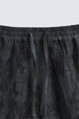 Bermuda de corte relajado, color gris oscuro con efecto tie-dye o textura irregular. Presenta cintura elástica ajustable con cordón y bolsillos laterales y traseros de plastrón.