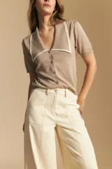 Pantalón largo color crema, tiro alto, de corte recto y ancho. Presenta costuras visibles en contraste y bolsillos delanteros.