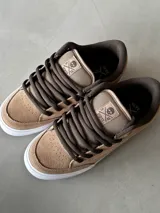 Championes de skate color beige con detalles en marrón, confeccionados en gamuza con puntera de triple costura, lengüeta acolchada con parche de la firma, ojales metálicos y suela vulcanizada blanca.