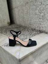 Sandalias negras de tacón bajo y ancho, con punta cuadrada, talón abierto y tira fina ajustable al tobillo.
