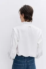 Blusa celeste de manga larga con puños fruncidos y elásticos, escote en V con cuello alto con volados y delicados bordados florales en el pecho.