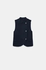 Top estilo chaleco de color azul marino, con cuello mao, sin mangas y trabillas en los hombros. Cuenta con cierre frontal cruzado mediante botones metálicos y bolsillos delanteros de plastrón con solapa.