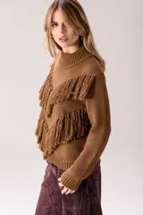 Sweater de punto color crema con cuello medio alto y silueta relajada. Presenta un diseño frontal con líneas en V decoradas con flecos largos de color marrón aplicados a mano.