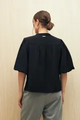 Blusa de color marrón con escote en V y mangas 3/4 con diseño acampanado. Presenta un sutil frunce en los hombros y una silueta relajada.