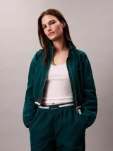 Campera tipo track Calvin Klein de tejido plano en color verde oscuro, de corte cropped y manga larga. Cuenta con cuello alto, cierre frontal de cremallera metálica, bolsillos laterales y elástico acanalado a rayas en los puños y el dobladillo. Presenta el logo de la marca bordado en el pecho.