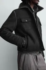 Cazadora cropped fit de tejido efecto piel en color marrón, con interior de borreguillo a tono. Presenta cuello solapa, cierre frontal con botones, bolsillos de plastrón en el pecho y bolsillos de vivo en la cadera.