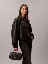 Cartera acolchada Calvin Klein de mano, color negro, con diseño matelassé en rombos, asa superior y correa de cadena metálica. Incluye pequeño logo metálico en la parte frontal.