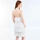Vestido corto blanco sin mangas, con cuello halter y diseño de volantes escalonados en capas superpuestas.