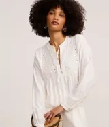 Blusa tipo bata de color blanco con mangas largas y cuello mandarín con lazo. Presenta detalles de bordado floral y calados tipo laise en el pecho.