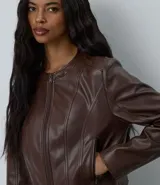 Campera de cuero sintético color marrón, con cuello redondo, cierre frontal y bolsillos laterales con cremallera. Presenta cortes verticales que estilizan la silueta.