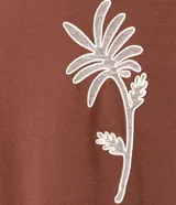 Remera marrón de corte regular, cuello redondo y manga corta, con estampa bordada de una palmera en el frente.