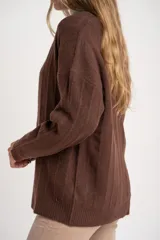 Cardigan de tejido de punto grueso color marrón oscuro, con escote en V y cierre frontal de botones redondos color hueso. Presenta un diseño texturado con líneas verticales marcadas.