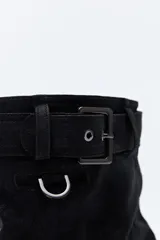 Bota de caña media color negro, con suela robusta dentada y detalle de hebilla ajustable en la parte superior. Presenta una argolla metálica lateral y un diseño de estética urbana con acabado texturizado.