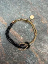 Pulsera de oro de 18k con diseño de cadena tipo serpiente doble y un nudo central decorativo. Cuenta con cierre de mosquetón y cadena de alargue con placa grabada.