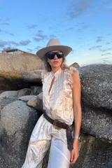 Conjunto de dos piezas confeccionado en seda plisada color beige. Incluye una blusa sin mangas con volados en los hombros y un pantalón de corte holgado con puños elásticos fruncidos en los tobillos.