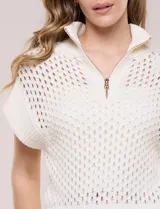 Buzo de punto color marfil, confeccionado en algodón calado con cuello alto acanalado y medio cierre metálico dorado. Presenta mangas cortas estilo japonesa con puños anchos y un zócalo acanalado en el ruedo.