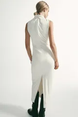 Vestido midi de color negro, sin mangas, con cuello subido y detalle de tejido drapeado en el lateral. Cuenta con cierre de cremallera oculta en la espalda.