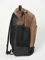 Mochila de color marrón claro y negro, con múltiples bolsillos frontales con cierre y logo de Rusty en negro. Presenta paneles laterales de malla negra y asa superior.