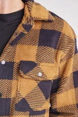 Camisa de abrigo de tela tipo borreguito a cuadros color marrón y negro, con cuello clásico, cierre frontal con botones a presión, bolsillo de parche en el pecho y puños abotonados.