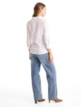 Camisa blanca de algodón con cuello camisero y escote en V. Presenta detalles plisados en el frente, cierre central con botones y mangas tres cuartos con puños abotonados. Los laterales están confeccionados en tejido modal para mayor comodidad.