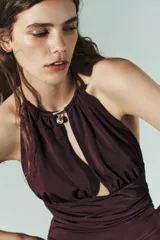 Body color borgoña de cuello halter con escote pronunciado, detalle de pieza metálica y aplicación joya. Tejido drapeado y cierre inferior con botones a presión y en cuello con gancho metálico.