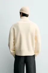 Jersey de punto color blanco con efecto pelo, cuello subido y cierre frontal de cremallera, de corte regular fit y manga larga con acabados en rib.