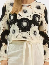 Buzo de tejido crochet con diseño de motivos circulares en contraste blanco y negro, con apliques de pedrería en el centro de los círculos. Presenta corte recto, cuello redondo y manga larga.