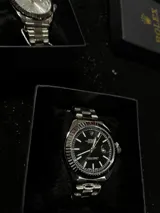 Reloj Rolex Datejust plateado con esfera negra, indicador de fecha y malla de acero inoxidable.