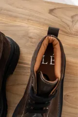 Borcegos de punta cuadrada con diseño acordonado, combinando paneles de cuero texturizado y gamuza en tonos marrones. Presentan una suela track gruesa de goma negra y cordones negros.