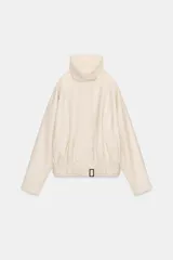 Chaqueta bomber oversize de efecto piel en color crema, con cuello subido, manga larga con hombro caído y cintura con frunces y cinturón ajustable con hebilla metálica. Cuenta con cierre frontal oculto y bolsillos laterales de vivo.