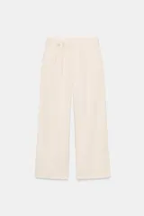 Pantalón ancho color beige claro, de tiro alto, con pinzas frontales, bolsillos delanteros y ajuste con lazo del mismo tejido en la cintura.