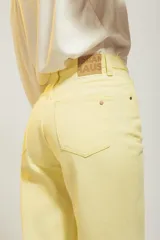 Pantalón de jean color amarillo pastel, de corte recto y tiro medio, con diseño de cinco bolsillos y cierre frontal con botón y cremallera.