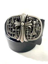 Cinto negro de cuero sintético con una hebilla metálica grande de diseño ornamentado con múltiples cruces estilo gótico.