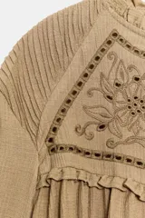 Camisa blanca de manga larga con cuello redondo y diseño abullonado, con detalle de bordados y encaje en la parte frontal y cierre de botón en la espalda.