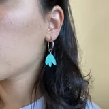 Par de aros plateados de acero quirúrgico hipoalergénico con dije colgante abstracto color naranja.