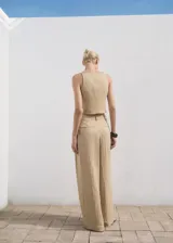 Pantalón Deia de corte recto y largo, color beige, con detalle de pinzas, trabillas y bolsillos laterales. Cuenta con cierre oculto de botón, gancho y cremallera, y forro interior.