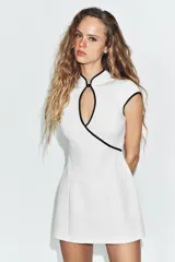 Vestido corto de escote cruzado con abertura frontal y cierre de botón, manga muy corta y detalle de vivos a contraste en color negro. Incluye forro interior tipo shorts y cierre de cremallera oculta en la espalda.