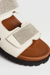 Sandalias planas color hueso, con doble tira con apliques de strass y ajuste con velcro.