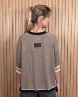 Buzo de punto negro con diseño holgado, mangas codo y detalles en tono tostado y blanco en el cuello redondo, puños y ruedo.