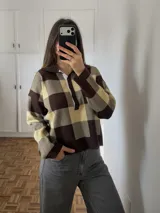 Sweater tejido de punto con estampado a cuadros grandes en color marrón y tostado, con cuello polo y cierre frontal de botones.