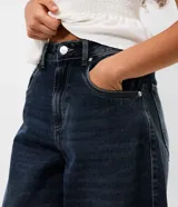 Pantalón de jean corte barrel con cintura media, trabillas para cinturón, bolsillos delanteros y traseros, cierre tradicional y detalle de recorte transversal en los laterales.