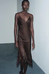 Vestido largo de satén con escote en pico y tirantes finos. Presenta aplicaciones de encaje a tono en el escote y en el lateral, con un bajo asimétrico.