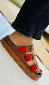 Sandalias de cuero marrón con tres tiras ajustables con hebillas doradas y detalles en rojo.