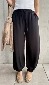 Pantalón negro tipo babucha con cintura elástica fruncida y cordón ajustable, corte holgado y puños elásticos en los tobillos.