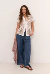 Camisa blanca de manga corta con cuello solapa, cierre frontal de botones y diseño bordado en hilo azul marino con motivos florales y vegetales.