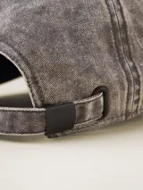 Gorra de béisbol color gris oscuro con efecto lavado o acid wash, visera curva y panel frontal estructurado. Presenta una pequeña etiqueta negra cosida en el lateral trasero.