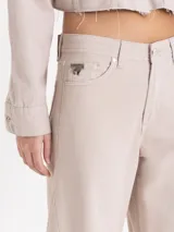 Pantalon de jean color beige, de corte wide leg con silueta redondeada y pinzas en las rodillas. Cuenta con cierre de botón y bragueta, bolsillos laterales y traseros, y detalles de remaches metálicos.